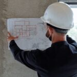 Engineer in hardhat reviewing architectural floor plans at construction site.